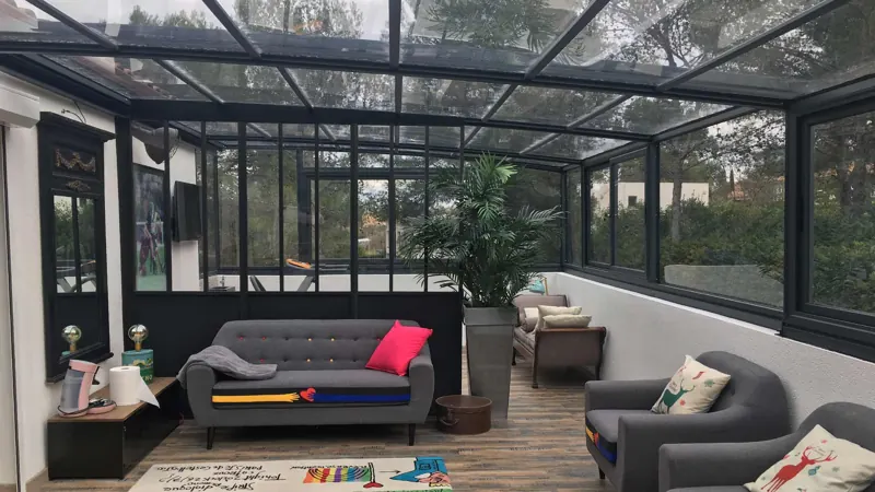 Abri de terrasse vitré à structure grise abritant un salon extérieur